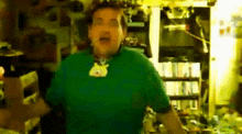 a man in a green shirt is standing in a kitchen with a cat on his neck .