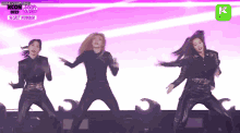 a group of women are dancing on a stage in front of a pink background .