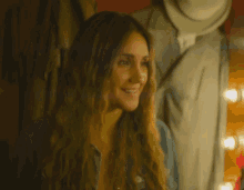 a woman with long hair is smiling in front of a mannequin in a dressing room .