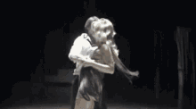 a man is holding a woman in his arms while they dance on a stage in a dark room .