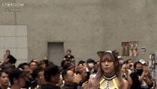 a woman stands in front of a crowd with the word stardom on the bottom left