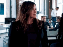 a woman in a black jacket is standing in an office with nbc on the bottom right
