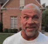 a bald man with a beard is making a funny face in front of a brick building