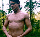 a shirtless man standing in the woods with his hands on his hips