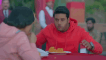 a man and a woman are sitting at a table with a plate of food . the woman is wearing a pink hoodie .