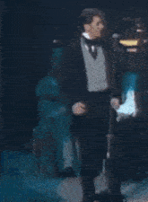 a man in a tuxedo is singing into a microphone on stage .