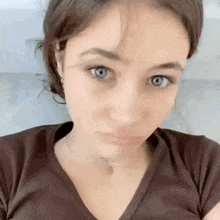 a close up of a woman 's face with blue eyes wearing a brown shirt and a cross necklace .