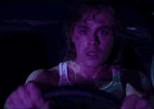 a man with a tattoo on his face is driving a car in a dark room