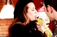 a woman is drinking from a bottle while a man holds a green bottle
