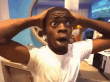 a man in a white shirt has his hands on his head and looks surprised