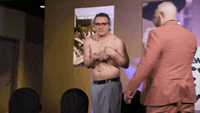 a shirtless man in a suit stands next to another man