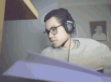 a young man wearing headphones and glasses is holding a piece of paper in his hand .
