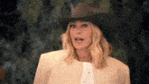 a woman wearing a cowboy hat and a white jacket is making a funny face .