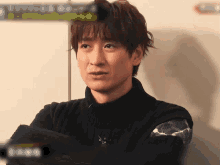 a man wearing a black sweater with his arms crossed looks at the camera