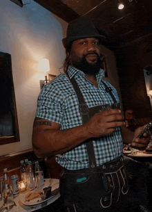 a man in a plaid shirt and suspenders holds a glass of beer