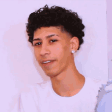 a young man with curly hair wearing a white shirt and earrings