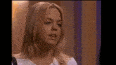 a woman with blonde hair is standing in front of a purple wall and talking to someone .
