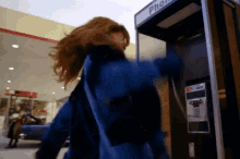 a woman in a blue jacket is standing next to a phone booth