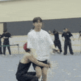 a man in a white shirt is holding another man in black shorts