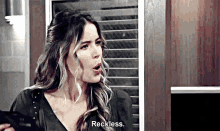 a woman is standing in a kitchen talking to a man and says `` reckless '' .