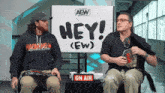 two men sit in front of a sign that says hey ( ew )