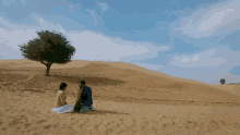 a man and a woman sit on the sand in the desert