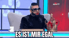 a man with a beard and sunglasses is sitting in front of a table with a crown on it .