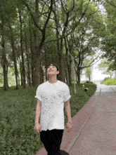 a man wearing a white t-shirt and a hat is walking down a path in the woods .