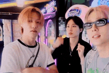 three young men wearing sunglasses are standing next to each other in front of a video game machine .