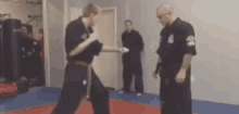 two men are practicing martial arts in a gym while a man stands in the background .