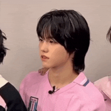 a young boy with black hair is wearing a pink shirt and a microphone .