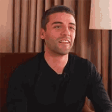 a man in a black shirt is smiling while sitting in a chair .