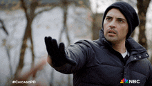a man wearing a black jacket and a black beanie with the nbc logo on the sleeve