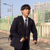 a man in a suit and tie is standing in front of a fence with a sign that says ' warning ' on it