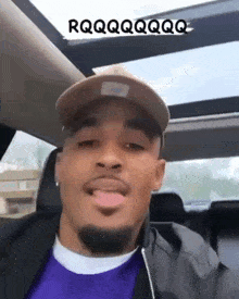 a man wearing a hat and a purple shirt is sitting in a car with the words rqqqqqqqq on the roof