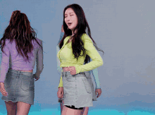 a woman in a green top and denim shorts stands next to another woman