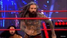 a wrestler with dreadlocks is standing in a wrestling ring with another wrestler .