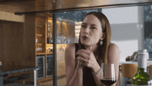 a woman is holding a glass of red wine and making a face