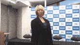 a woman in a suit stands in front of a shosen backdrop