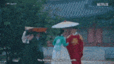 a man is holding an umbrella over a woman in a traditional korean dress .