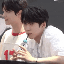 a man is drinking water through a straw while sitting next to another man .