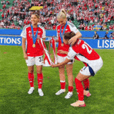 three female soccer players holding a trophy with the number 32 on their jersey