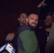 a man with a beard is standing in front of a group of men in a dark room .