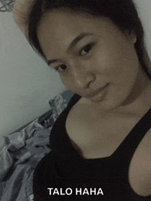 a woman in a black tank top is laying on a bed with the words talo haha above her