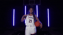 a woman in a uconn jersey is holding a basketball and pointing at the camera