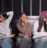 three women are sitting in a row with one wearing a hat with the letter b on it