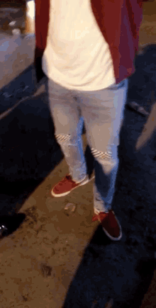 a person wearing ripped jeans and red shoes is standing on the sidewalk