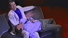 a man in a white suit is sitting on a couch next to another man .