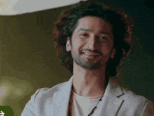 a man with curly hair and a beard is smiling while wearing a white jacket .