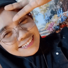 a woman wearing glasses and a hijab is smiling while making a peace sign .